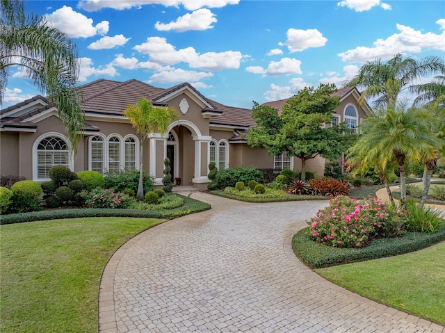 mediterranean / spanish-style house featuring a tile roof, a front yard, decorative driveway, and stucco siding