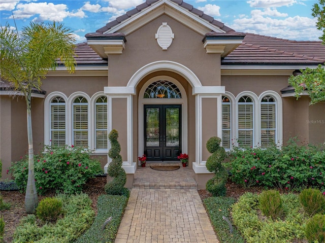 property entrance with a tiled roof, french doors, and stucco siding