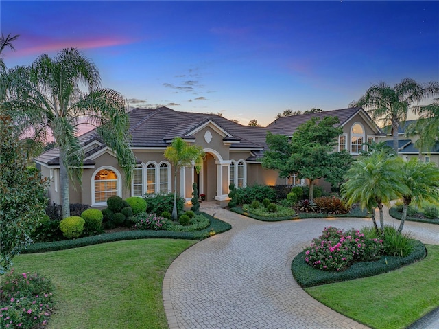 mediterranean / spanish-style home with a tile roof, curved driveway, a front lawn, and stucco siding