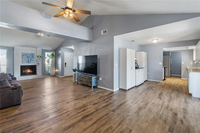 unfurnished living room with sink, vaulted ceiling, ceiling fan, a fireplace, and light hardwood / wood-style floors