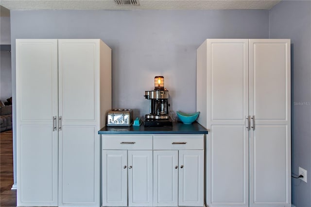 bar with white cabinetry and a textured ceiling