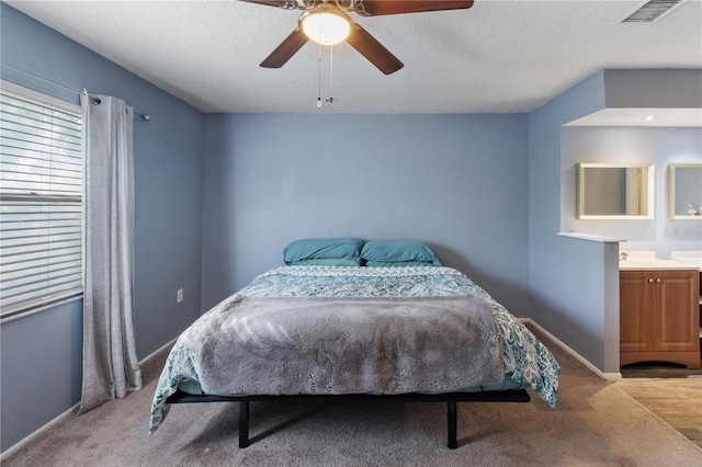 bedroom featuring ceiling fan, a textured ceiling, light carpet, and ensuite bath