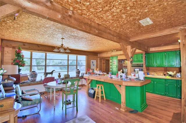 kitchen with dark wood-type flooring, hanging light fixtures, green cabinetry, beamed ceiling, and a kitchen island