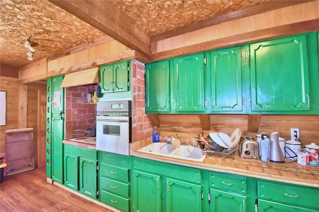 kitchen with oven, sink, wooden walls, green cabinetry, and hardwood / wood-style flooring