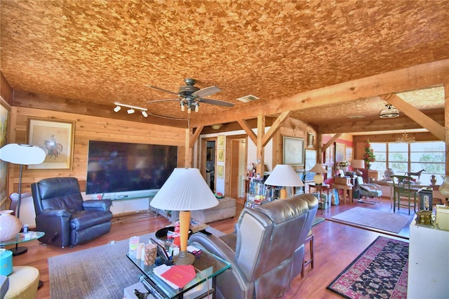 living room with beam ceiling, wooden walls, hardwood / wood-style floors, and ceiling fan