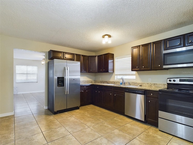 kitchen featuring sink, light tile patterned floors, light stone counters, dark brown cabinetry, and stainless steel appliances