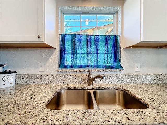 room details featuring light stone counters, white cabinetry, and sink