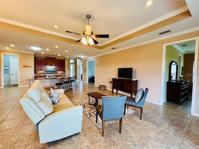 living room featuring a raised ceiling, ceiling fan, and crown molding