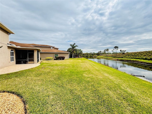 view of yard featuring a sunroom, a patio area, and a water view