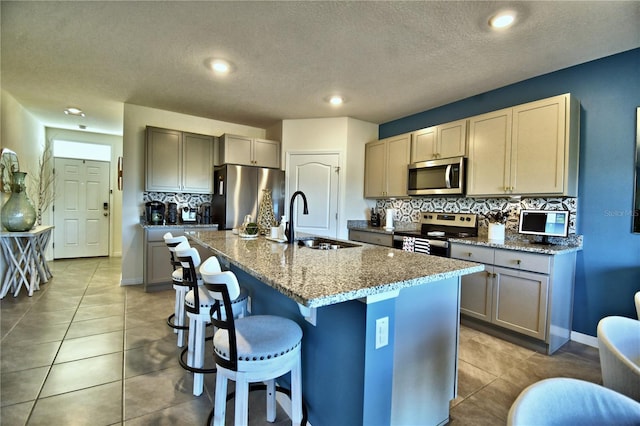 kitchen featuring sink, tasteful backsplash, dark stone counters, a center island with sink, and appliances with stainless steel finishes