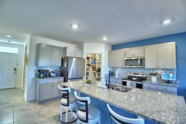 kitchen with light stone countertops, appliances with stainless steel finishes, backsplash, a breakfast bar area, and an island with sink