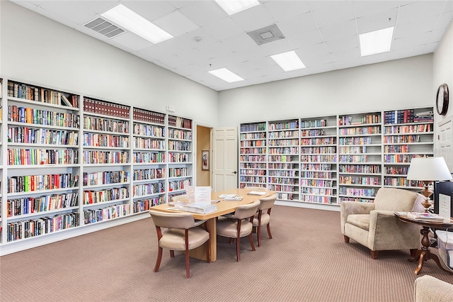 living area with wall of books, visible vents, a drop ceiling, and carpet flooring