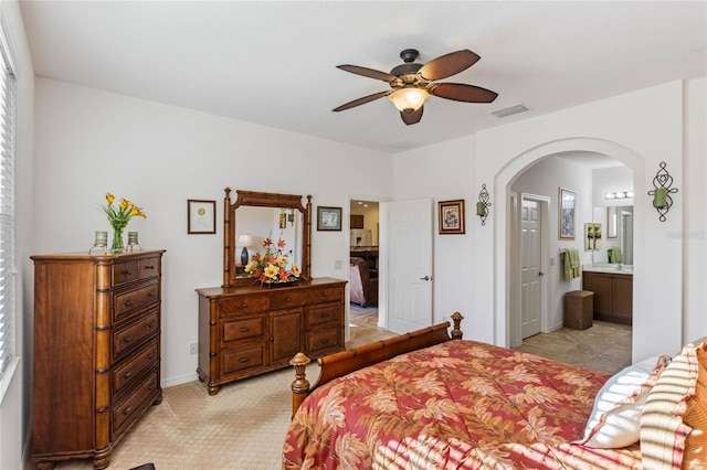 bedroom with arched walkways, ceiling fan, light carpet, visible vents, and ensuite bath