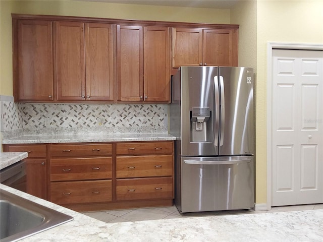 kitchen featuring light stone counters, backsplash, light tile patterned flooring, and stainless steel refrigerator with ice dispenser