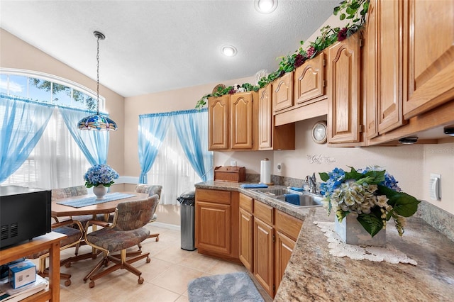 kitchen with sink, hanging light fixtures, light stone counters, a textured ceiling, and light tile patterned flooring