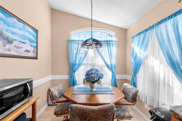 dining room with light tile patterned floors, a textured ceiling, and lofted ceiling