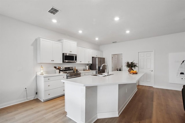 kitchen with white cabinets, a center island with sink, stainless steel appliances, light wood-type flooring, and sink