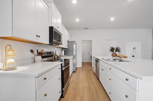 kitchen with stainless steel appliances, sink, white cabinetry, light wood-type flooring, and a kitchen island with sink