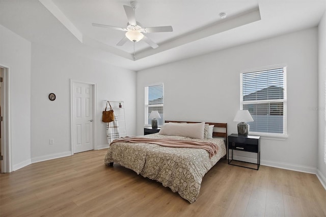 bedroom with light wood-type flooring, a raised ceiling, and ceiling fan