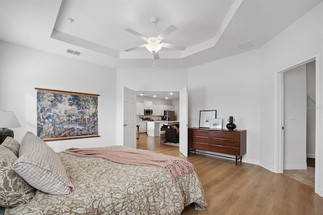 bedroom with ceiling fan, stainless steel fridge, light hardwood / wood-style flooring, and a raised ceiling