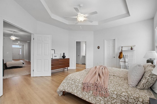 bedroom with ceiling fan, light hardwood / wood-style floors, and a raised ceiling