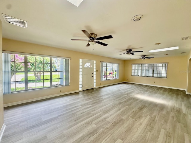 unfurnished living room featuring light wood-type flooring, a skylight, and ceiling fan