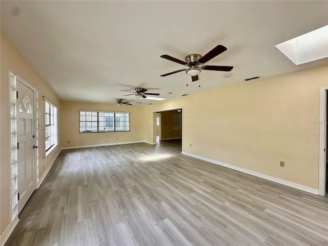 unfurnished room featuring a skylight, ceiling fan, and light wood-type flooring