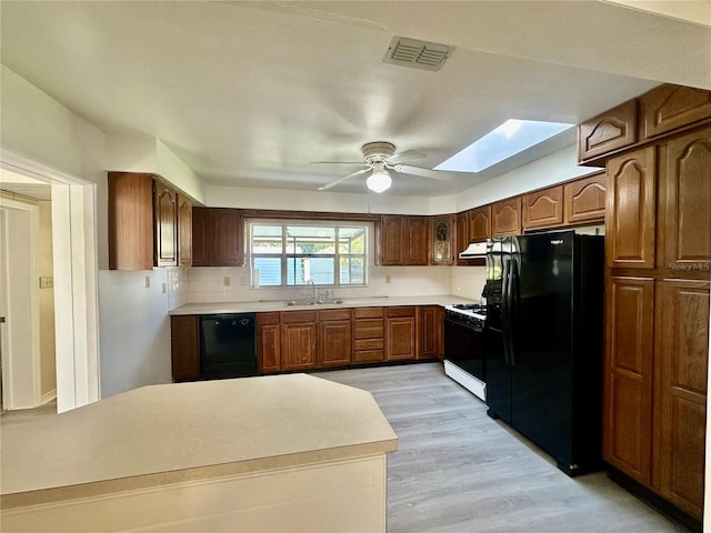 kitchen with a skylight, ceiling fan, sink, black appliances, and light hardwood / wood-style flooring