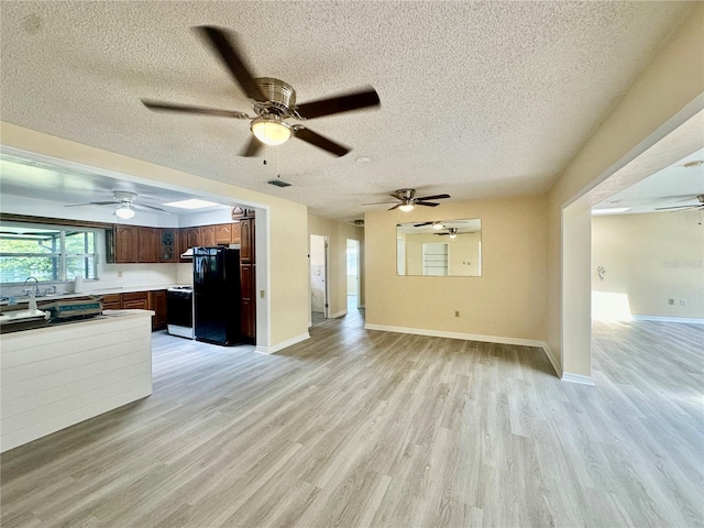 kitchen with black fridge, a textured ceiling, sink, light hardwood / wood-style flooring, and range