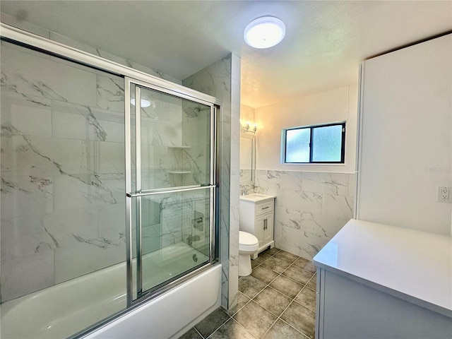 full bathroom featuring vanity, bath / shower combo with glass door, tile patterned flooring, toilet, and tile walls