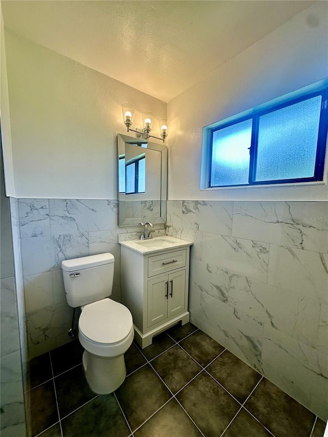 bathroom with tile patterned flooring, vanity, toilet, and tile walls