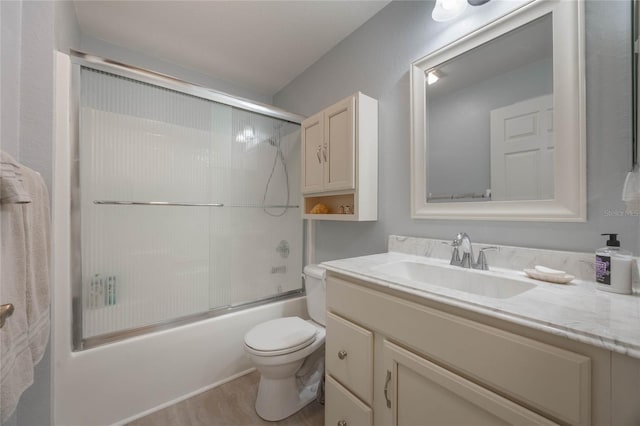 full bathroom with toilet, wood-type flooring, vanity, and bath / shower combo with glass door