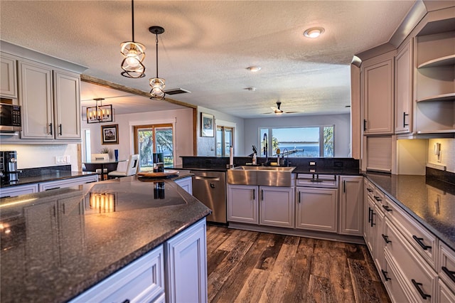 kitchen featuring sink, ceiling fan with notable chandelier, dark stone counters, hanging light fixtures, and appliances with stainless steel finishes