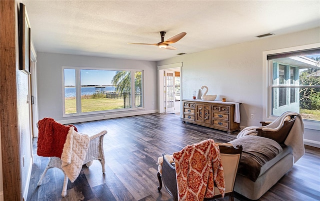 living room with a textured ceiling, dark hardwood / wood-style floors, ceiling fan, and a water view