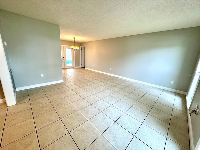 empty room featuring light tile patterned flooring, a textured ceiling, and a chandelier