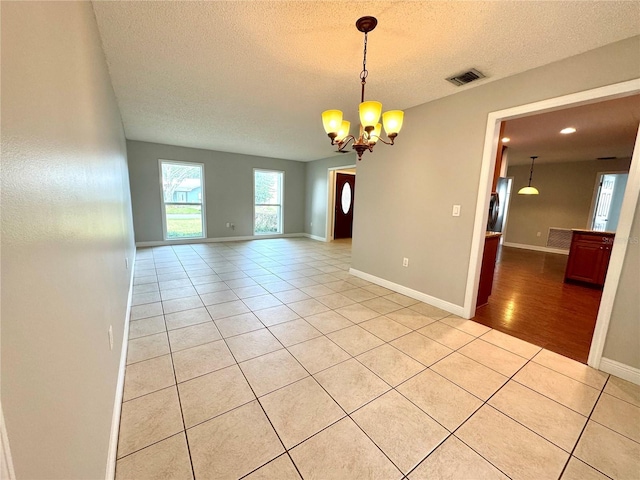 empty room featuring light tile patterned floors, a textured ceiling, and a chandelier