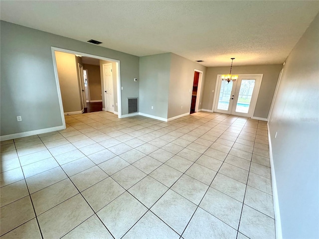 tiled spare room featuring a notable chandelier, french doors, and a textured ceiling