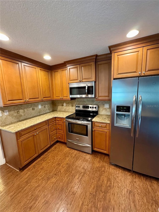 kitchen featuring appliances with stainless steel finishes, light wood-type flooring, backsplash, light stone countertops, and a textured ceiling