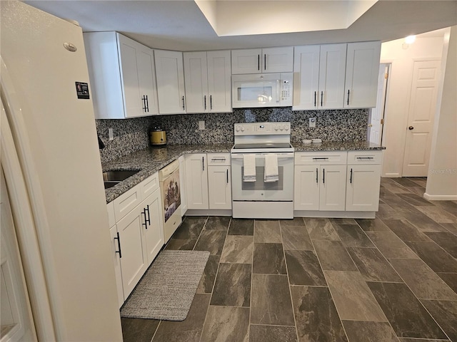 kitchen featuring backsplash, white appliances, a tray ceiling, dark stone countertops, and white cabinetry