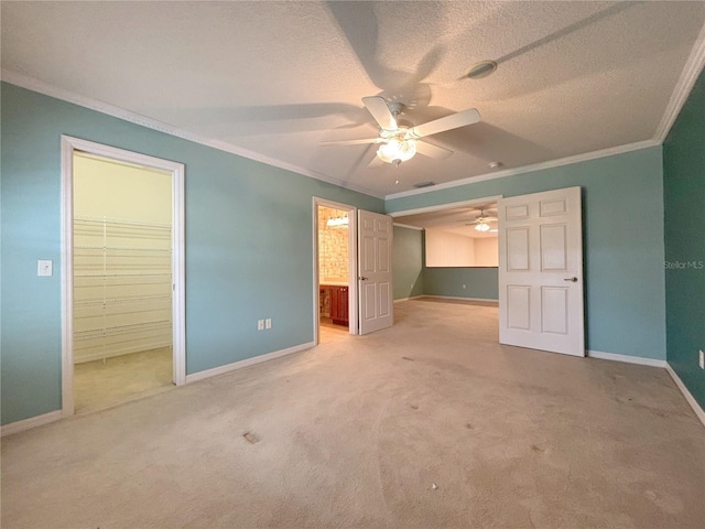 unfurnished bedroom with ceiling fan, ensuite bath, crown molding, a walk in closet, and a closet