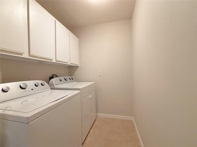 clothes washing area with light tile patterned floors, washer and dryer, and cabinets