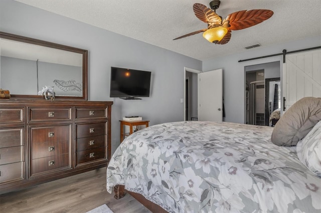 bedroom featuring ceiling fan, light hardwood / wood-style floors, a textured ceiling, and a barn door