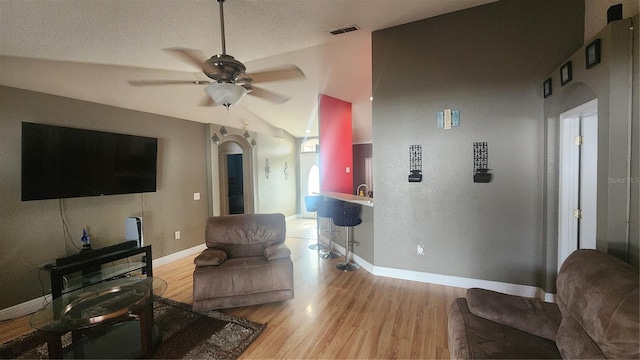 living room with a textured ceiling, ceiling fan, vaulted ceiling, and light hardwood / wood-style flooring