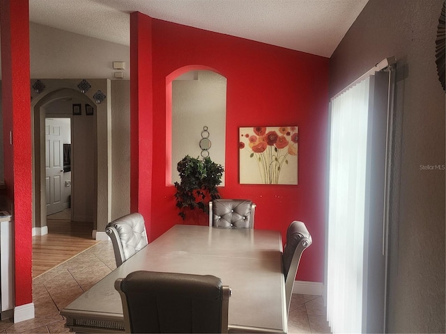 tiled dining area with vaulted ceiling and a textured ceiling