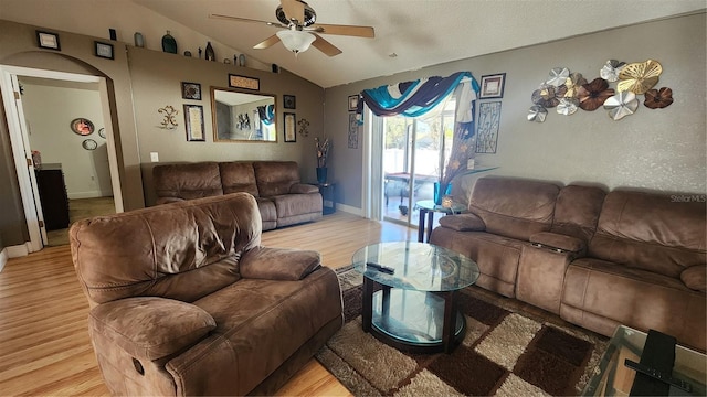 living room with arched walkways, light wood-style floors, ceiling fan, and vaulted ceiling