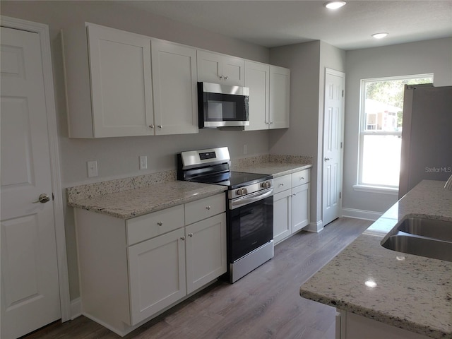 kitchen featuring white cabinetry, appliances with stainless steel finishes, light wood-type flooring, and light stone counters