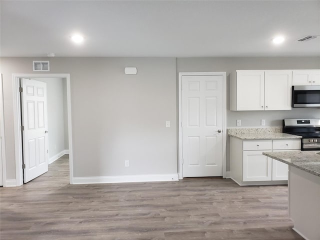 kitchen featuring light stone counters, stainless steel appliances, white cabinets, and light wood-type flooring