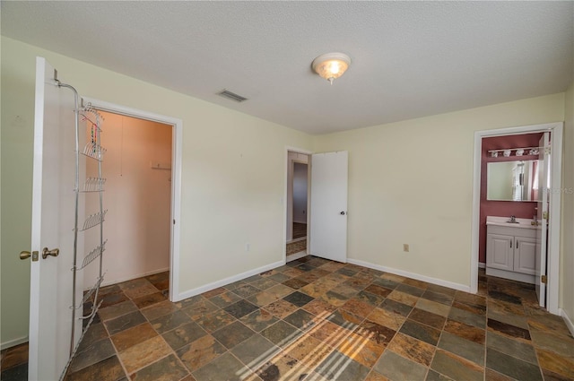 unfurnished bedroom featuring a textured ceiling, a spacious closet, ensuite bathroom, and a closet