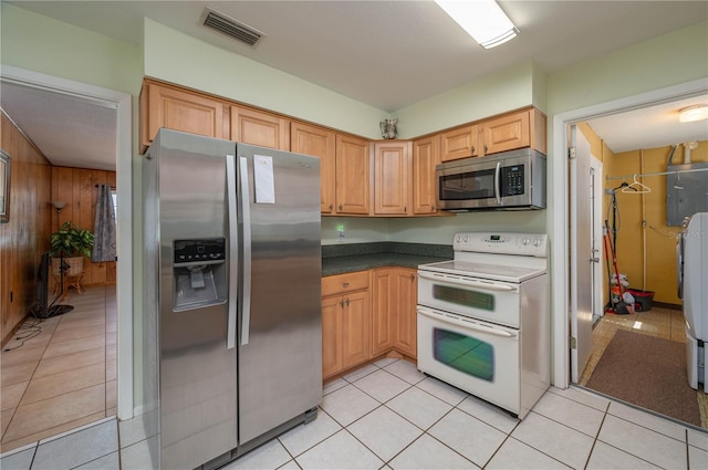 kitchen with appliances with stainless steel finishes, light tile patterned floors, wood walls, and electric panel