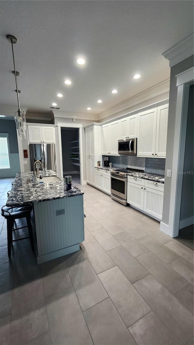 kitchen featuring appliances with stainless steel finishes, kitchen peninsula, dark stone counters, pendant lighting, and white cabinets